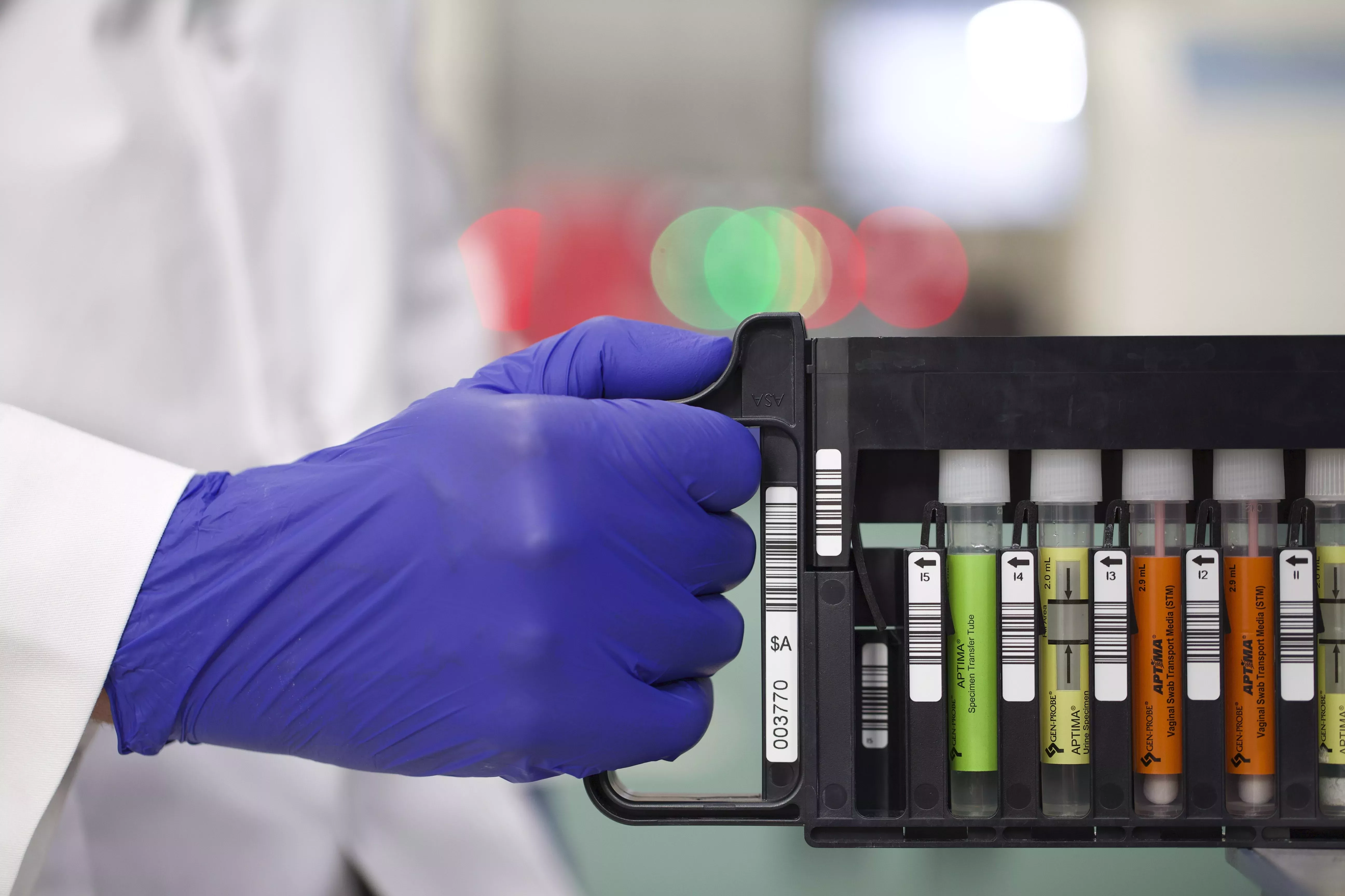 Gloved hand holds rack of vials in lab setting.