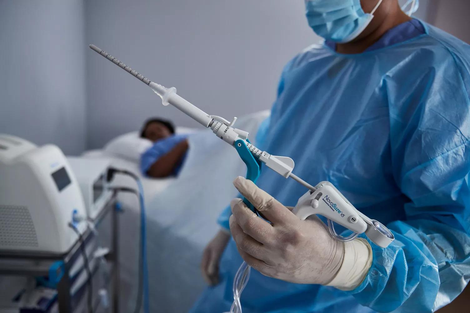 A surgeon is holding a NovaSure device next to a patient.